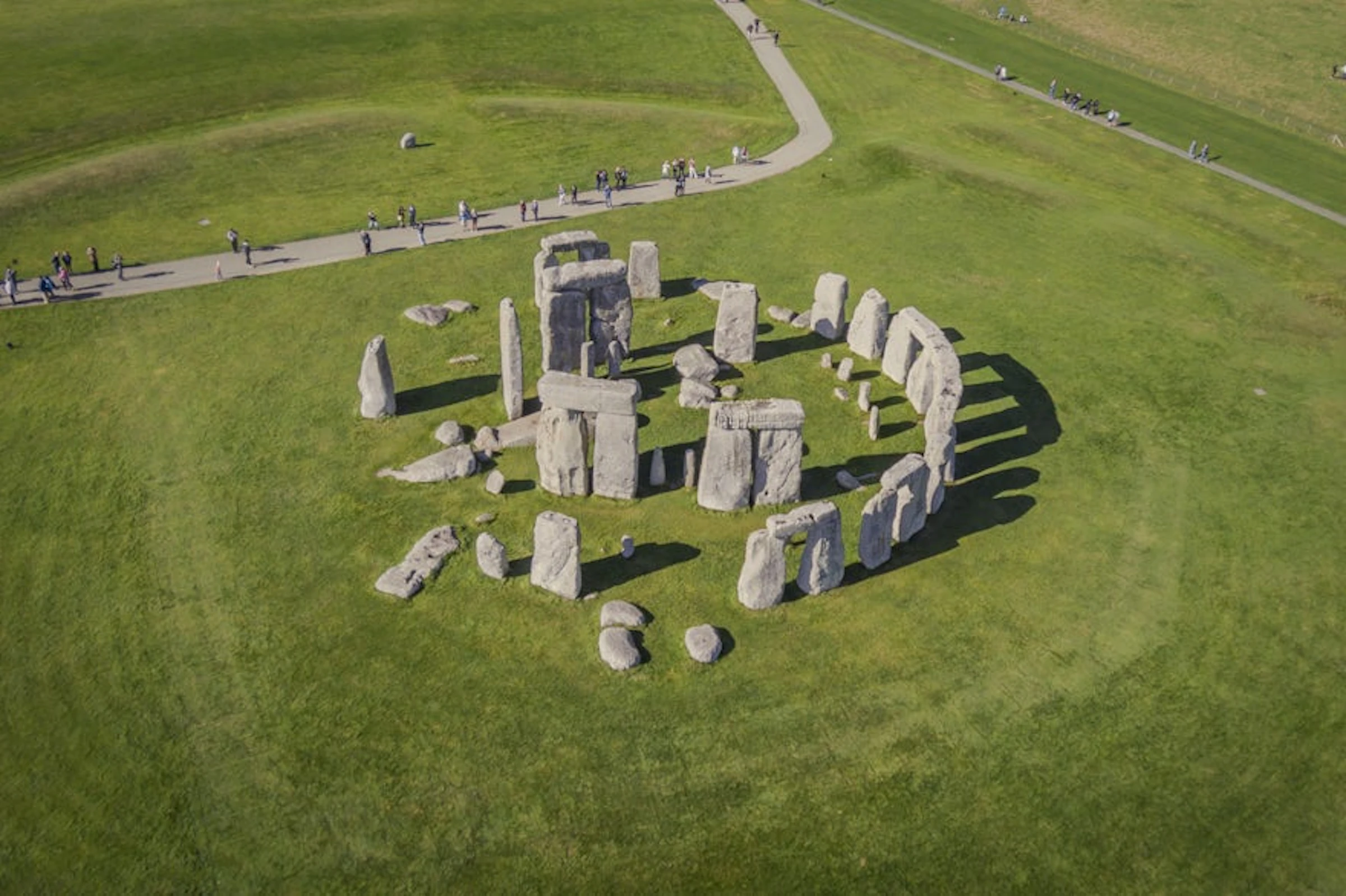 Aerial view of Stonehenge stone circle on green grass, with people walking on a nearby path.