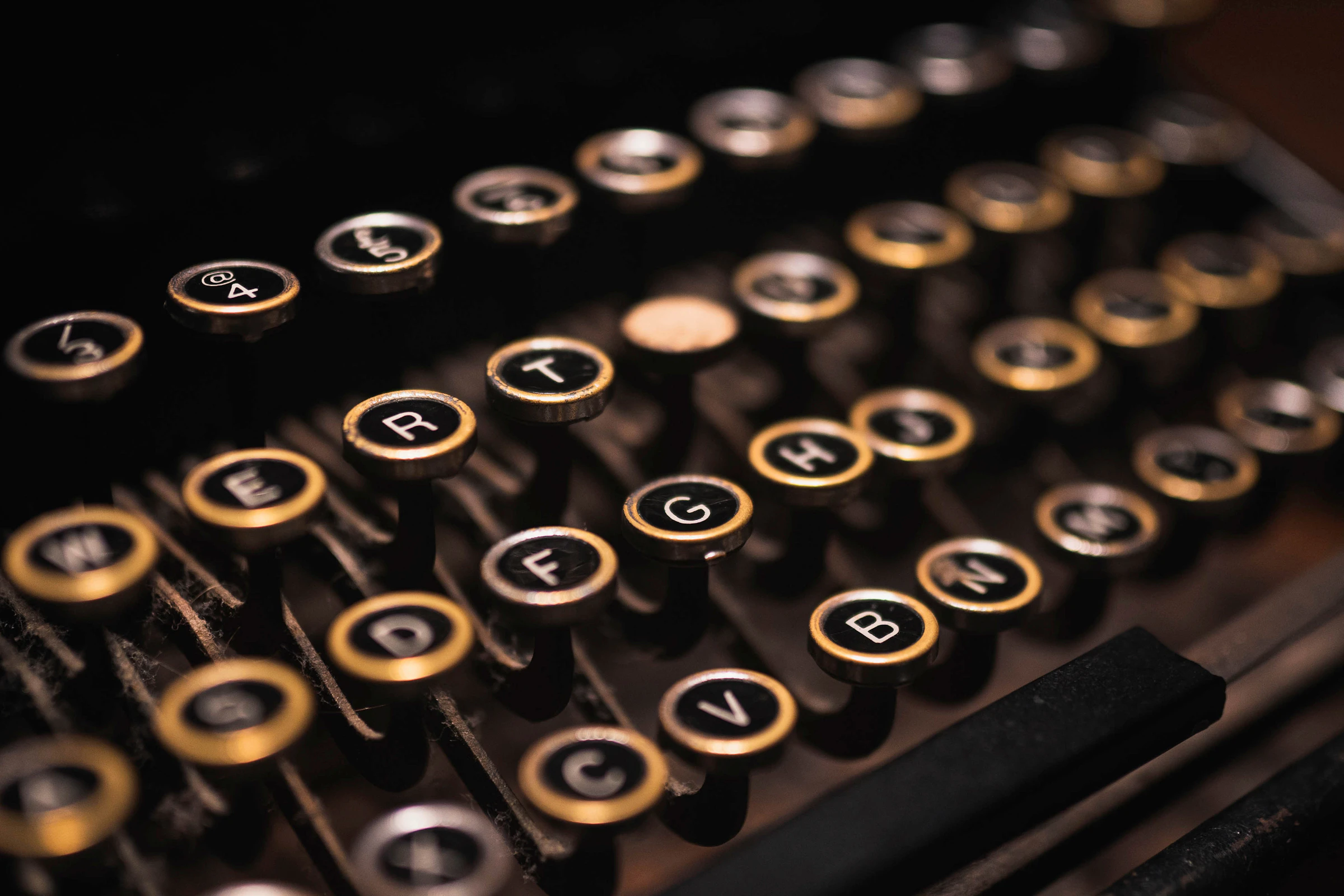 Close-up of vintage typewriter keys, with round black buttons and gold rims arranged in rows.