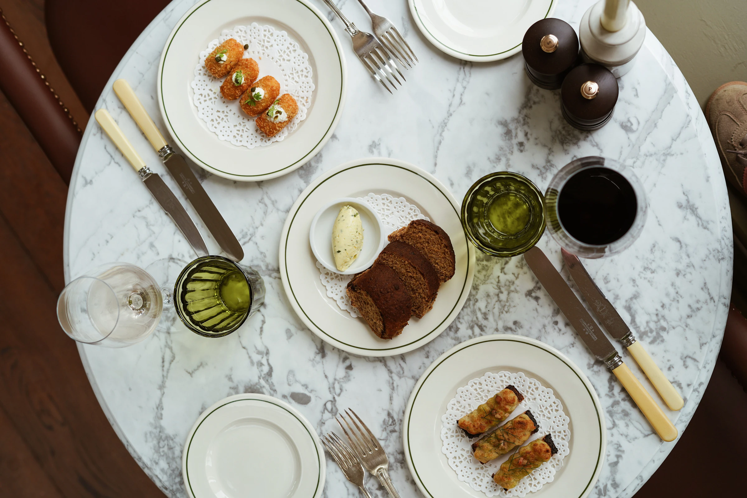 Marble table with plates of appetizers, bread with dip, two drinks, and cutlery set for two people.