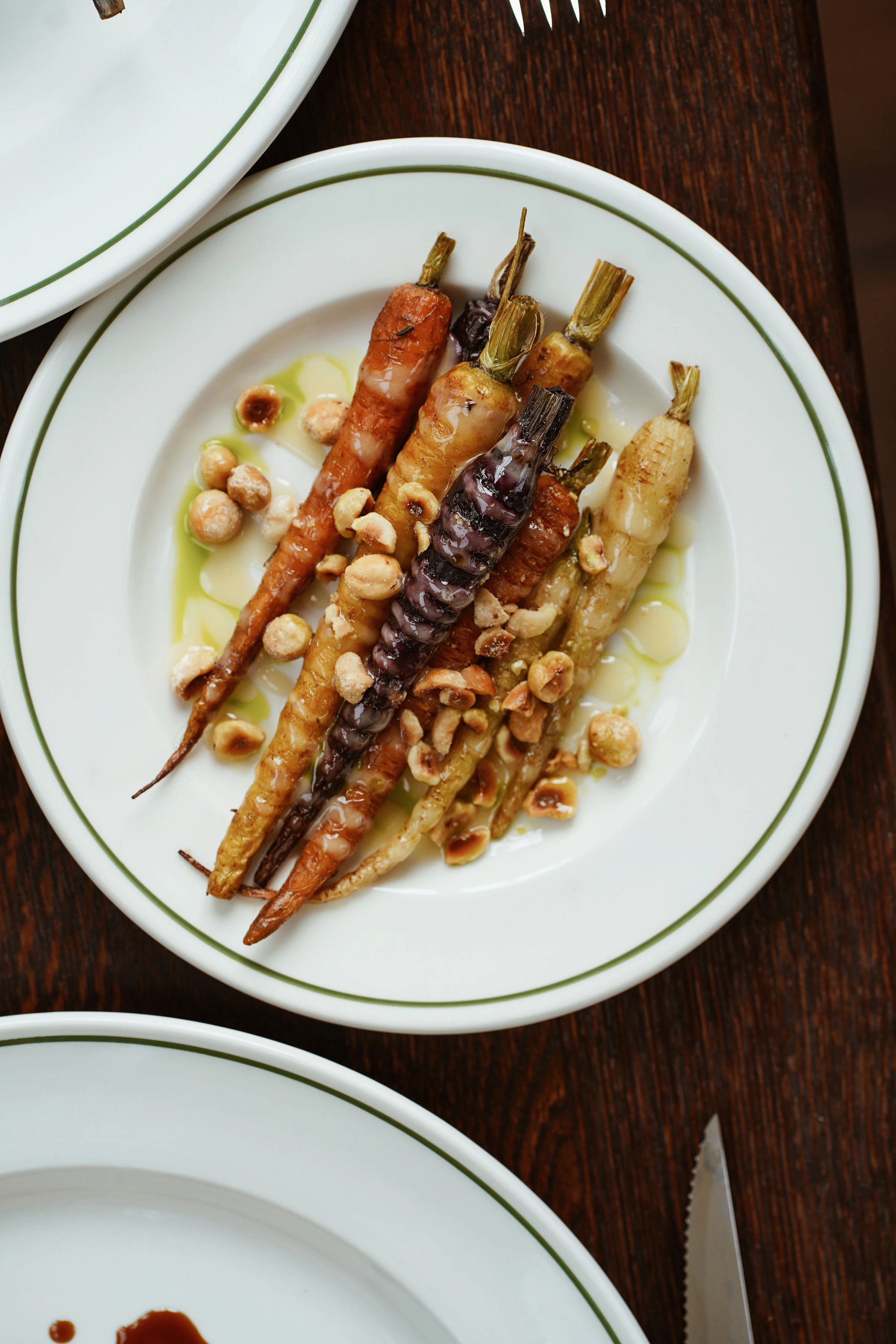 A plate of roasted multicolored carrots topped with nuts, served on a white plate with a green rim.