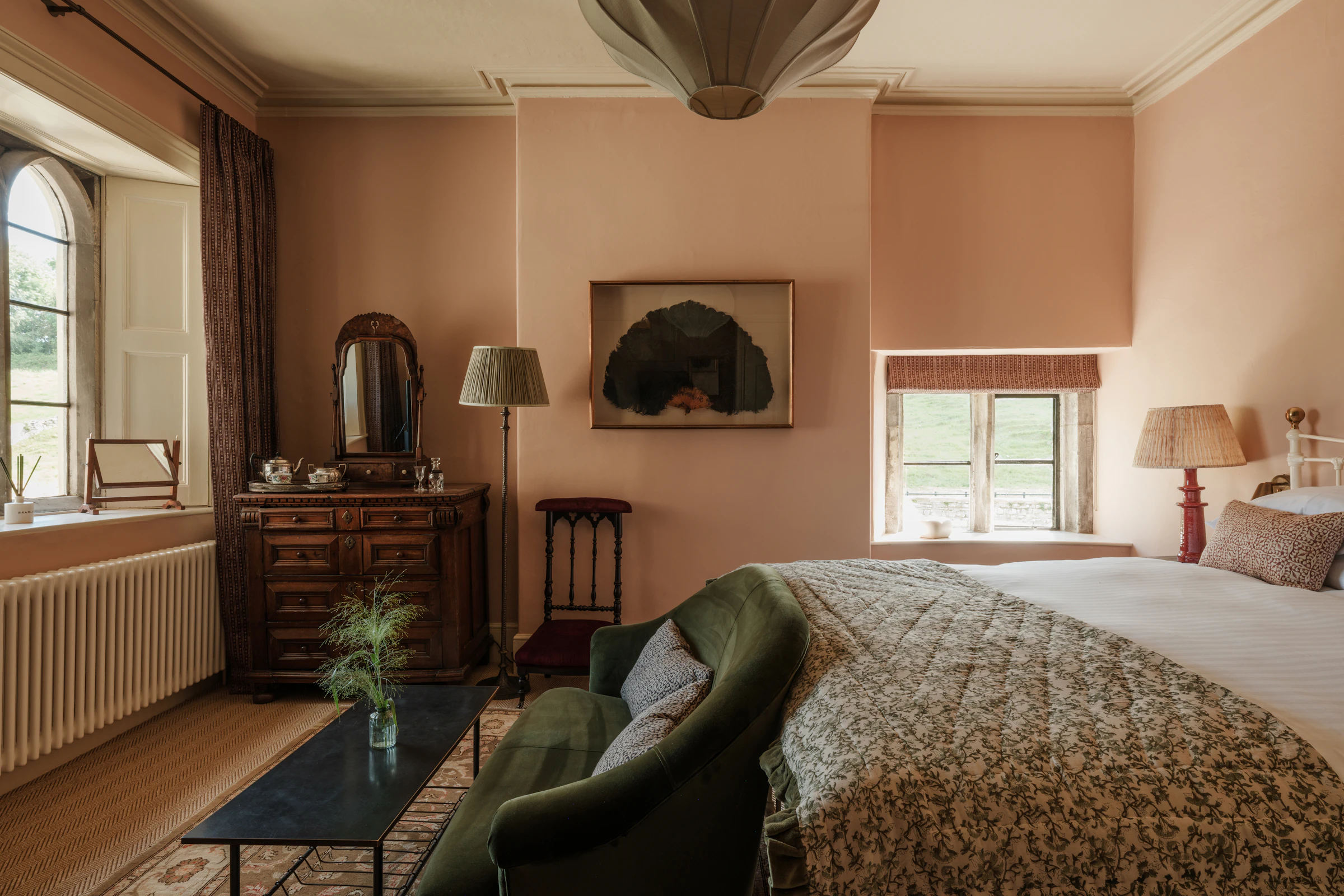 Cozy bedroom with a double bed, green sofa, vintage dresser, and large windows letting in natural light.