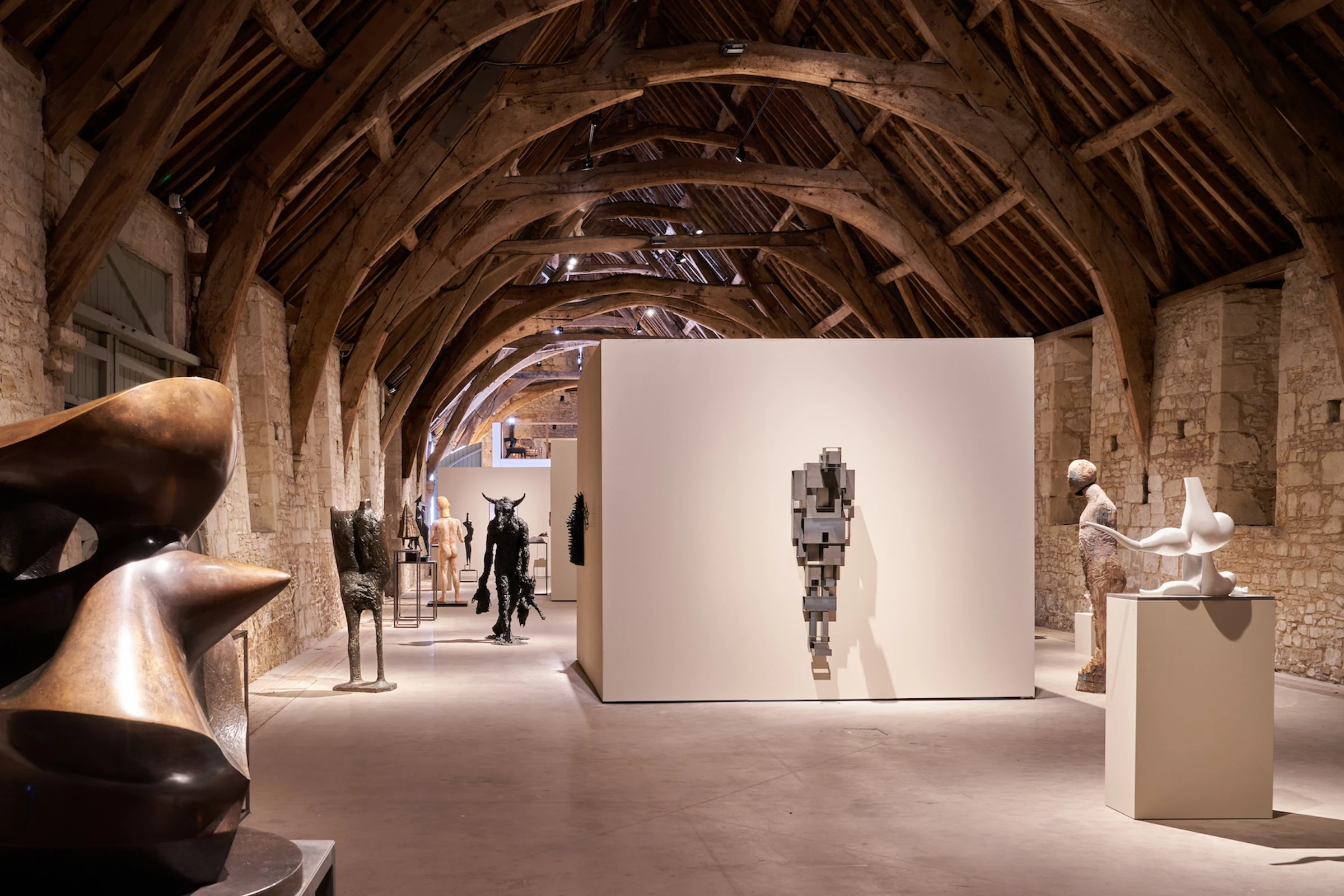 Sculptures displayed in a rustic gallery with stone walls and a vaulted wooden ceiling.