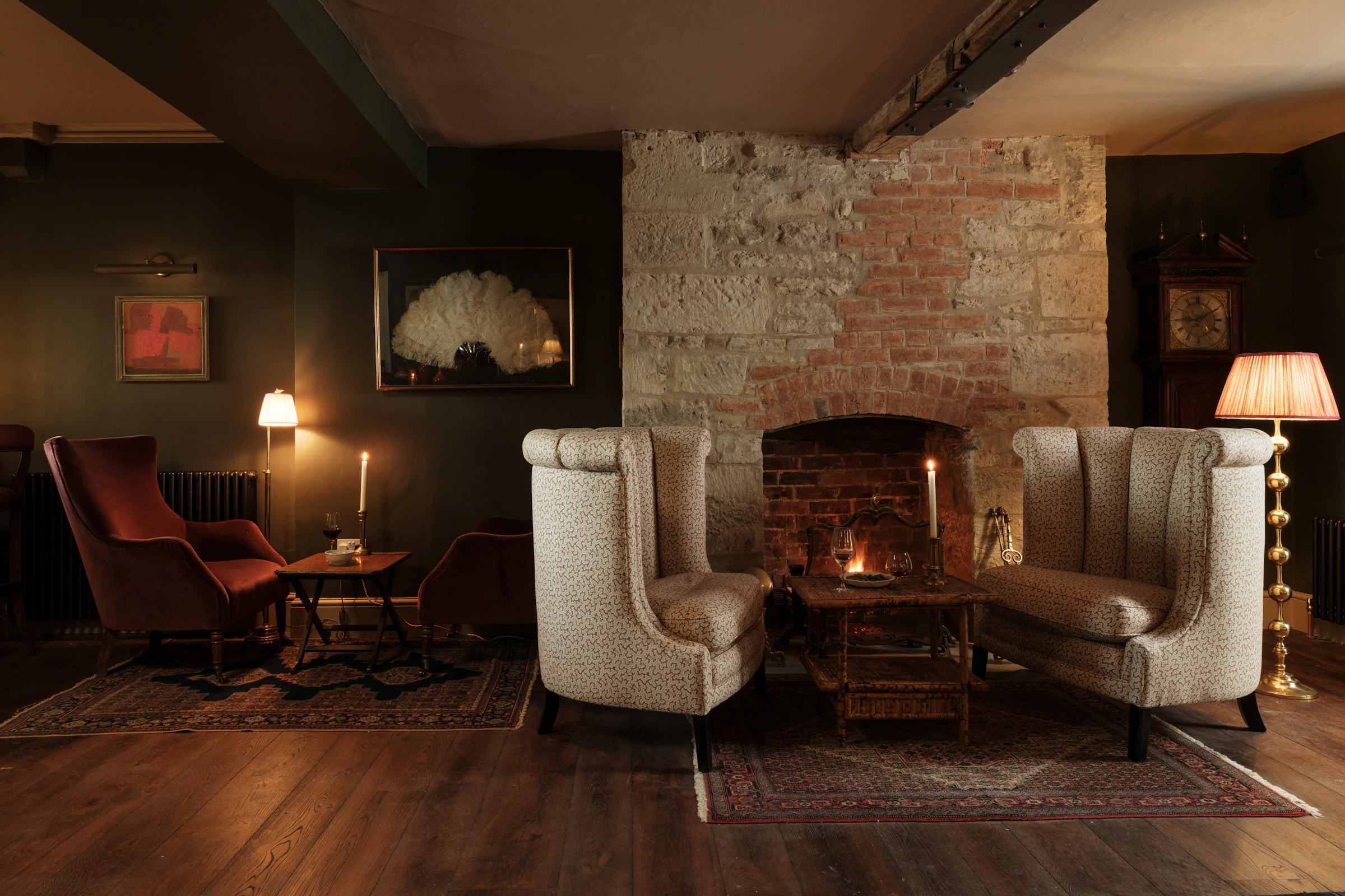 Cozy living room with armchairs, vintage rugs, a lit fireplace, soft lighting, and rustic brick and stone walls.